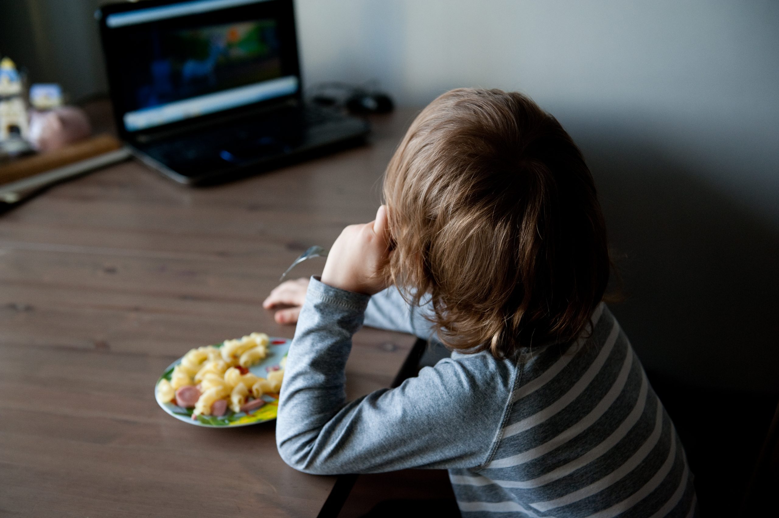 Enfant déjeunant en regardant l'écran d'un ordinateur portable