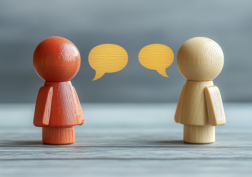 Deux figurines en bois se faisant face avec deux bulles jaunes symbolisant le dialogue, la communication et l'interaction sur un fond neutre. crédits photo : AdobeStock 